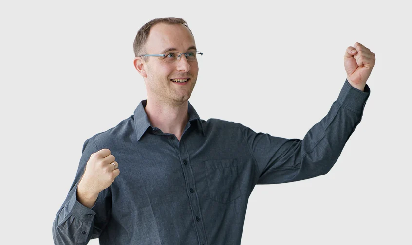 Toni mit grauem Hemd jubelt und hebt die Fäuste vor Freude über ein erfolgreiches Ergebnis