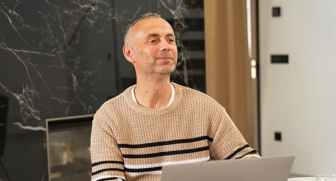 Sylvio sitzt am Schreibtisch mit Laptop und lächelt während eines Gesprächs