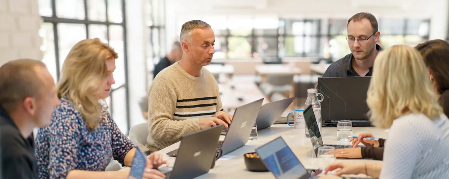 Team der SEO Revolution GmbH bei einer Besprechung am Konferenztisch, mehrere Personen arbeiten konzentriert an Laptops in einem modernen, hellen Büro.