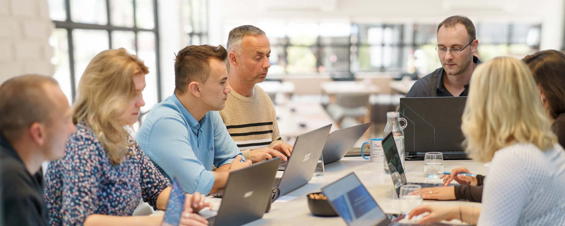 Team der SEO Revolution GmbH bei einer Besprechung am Konferenztisch, mehrere Personen arbeiten konzentriert an Laptops in einem modernen, hellen Büro.
