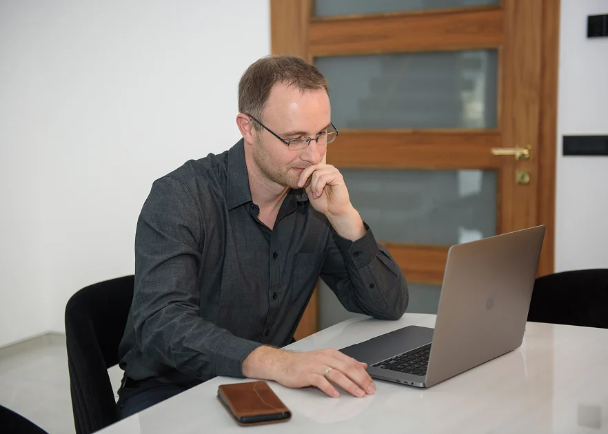 Mann arbeitet konzentriert am Laptop in modernem Büro mit Holztür im Hintergrund