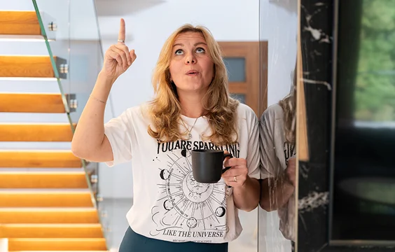 Valeria mit Kaffeetasse zeigt mit dem Finger nach oben und lächelt überrascht